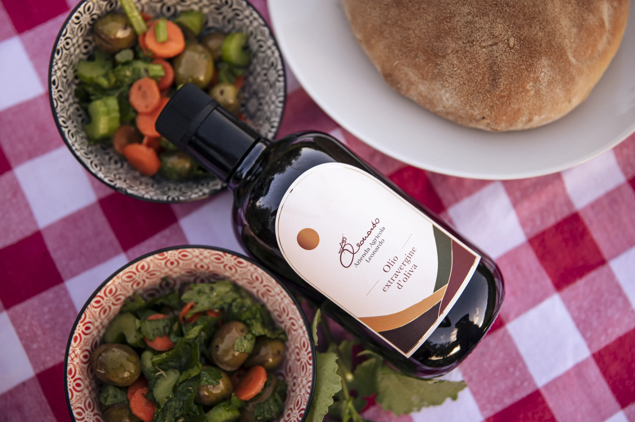 Bottiglia di Olio del Belice su tavola siciliana con pane e verdure fresche